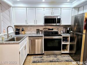Kitchen with crown molding, white cabinets, sink, and appliances with stainless steel finishes