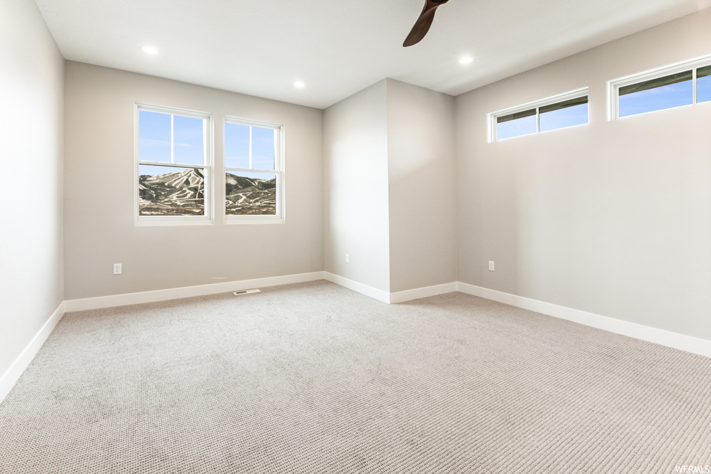 Spare room featuring ceiling fan, a wealth of natural light, and light carpet