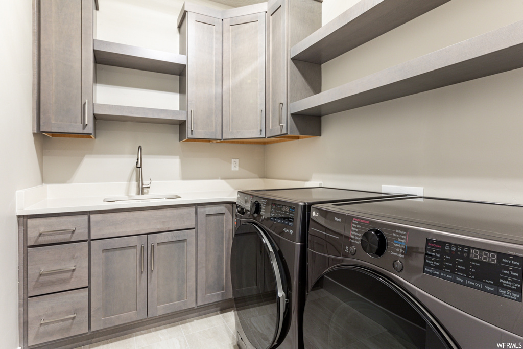 Laundry room with cabinets, washing machine and clothes dryer, sink, and light tile floors