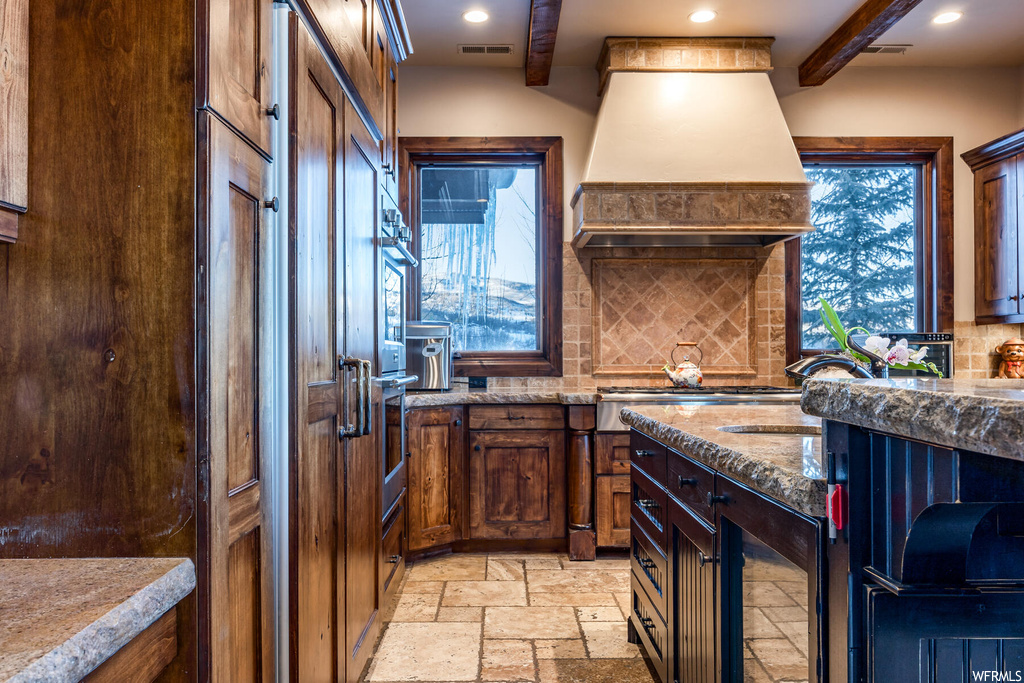 Kitchen with premium range hood, light tile flooring, stainless steel oven, beamed ceiling, and backsplash
