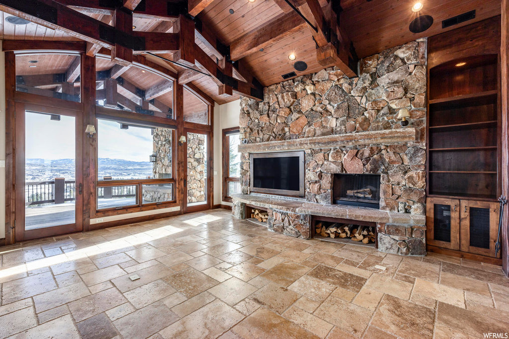 Unfurnished living room with beamed ceiling, a stone fireplace, a mountain view, light tile floors, and wooden ceiling