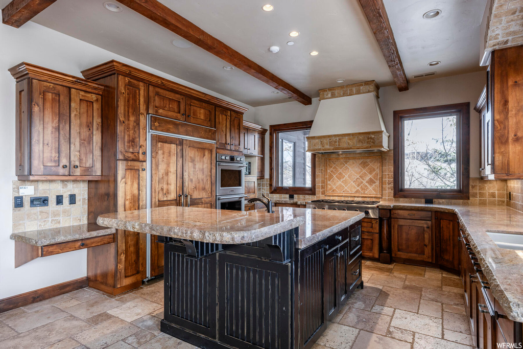 Kitchen with a center island with sink, premium range hood, beam ceiling, and backsplash