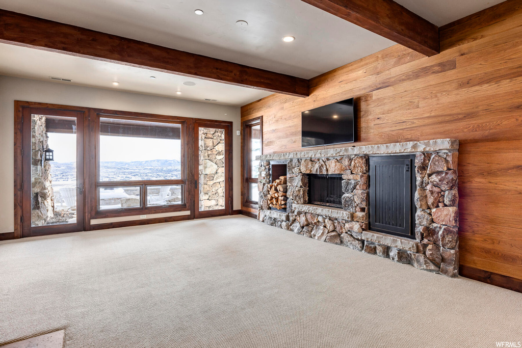 Unfurnished living room featuring light colored carpet, a fireplace, and beam ceiling
