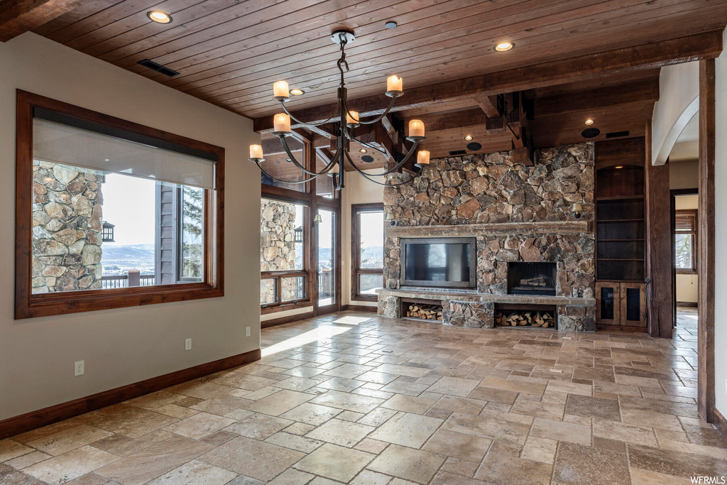 Unfurnished living room featuring wood ceiling, a chandelier, a stone fireplace, light tile floors, and beam ceiling