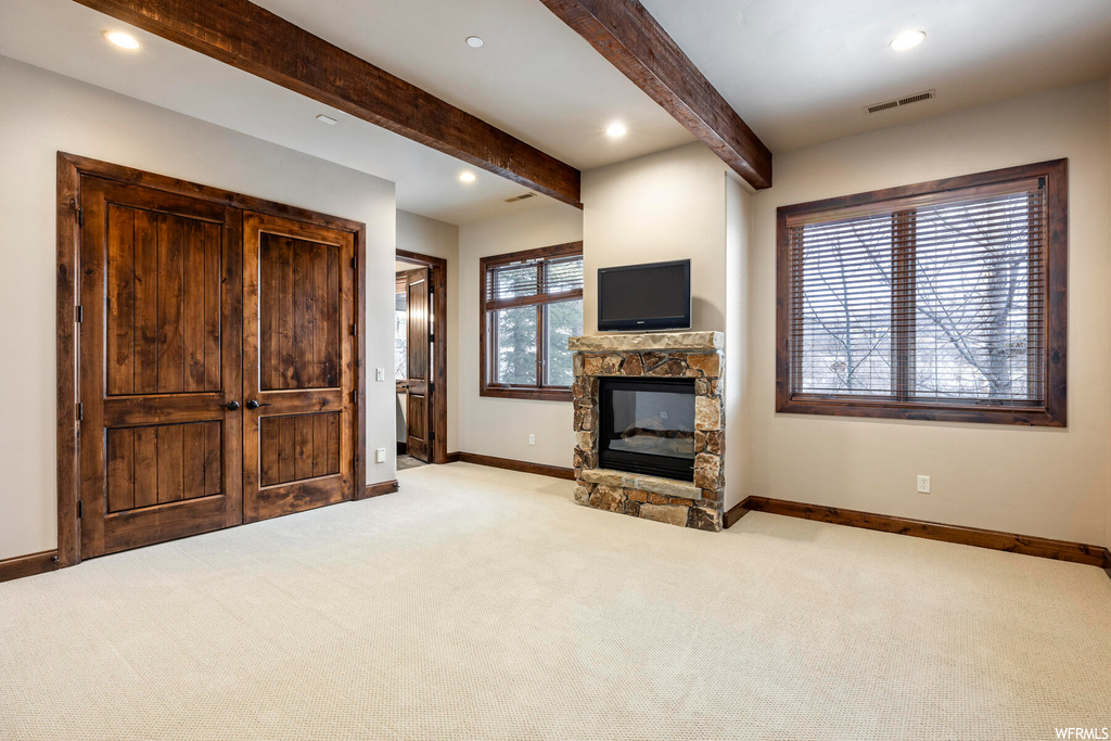 Unfurnished living room featuring light colored carpet, beam ceiling, and a stone fireplace