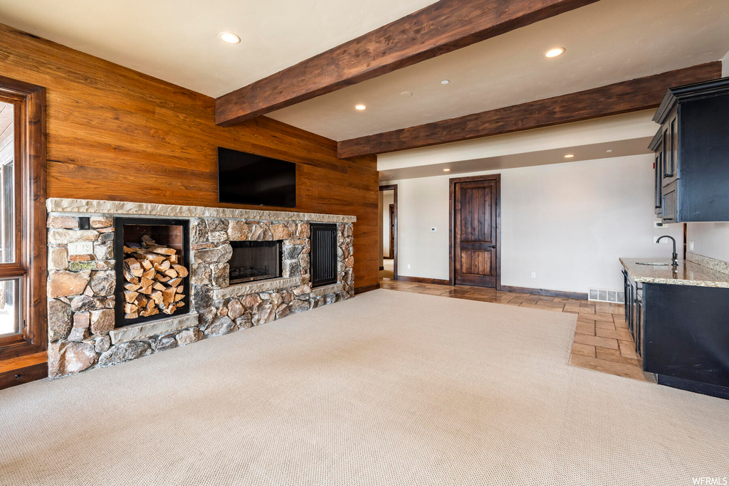 Unfurnished living room with light carpet, sink, beam ceiling, and a fireplace