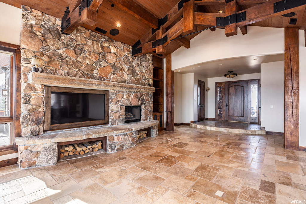 Unfurnished living room with wood ceiling, high vaulted ceiling, a stone fireplace, light tile floors, and beam ceiling