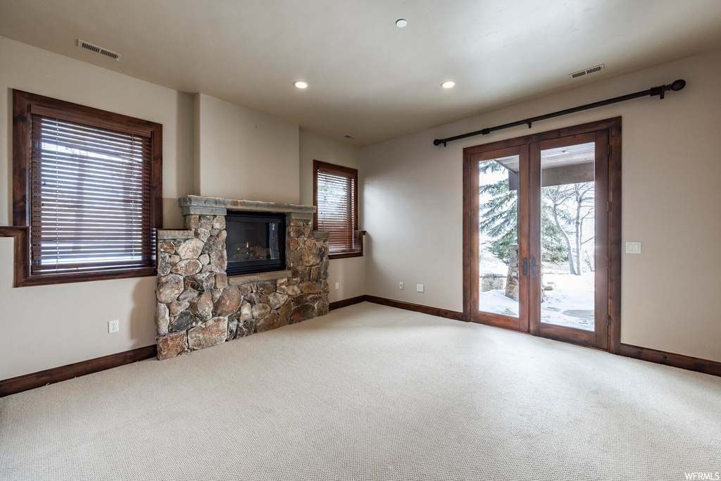 Unfurnished living room featuring light colored carpet and a stone fireplace