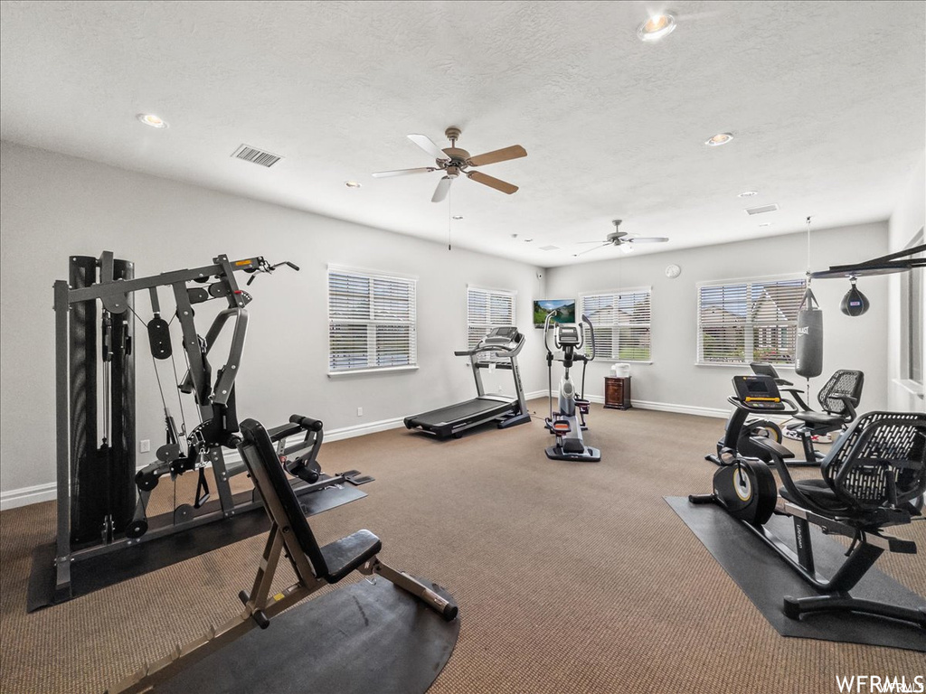 Workout area featuring dark colored carpet, ceiling fan, and a textured ceiling