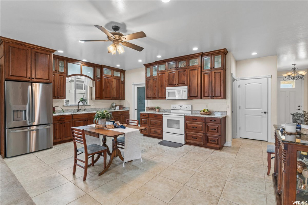 Kitchen featuring sink, white appliances, ceiling fan with notable chandelier, light tile flooring, and light stone countertops
