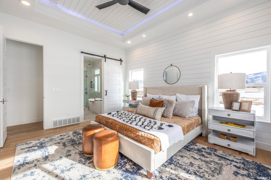 Bedroom featuring multiple windows, light wood-type flooring, ceiling fan, and a barn door