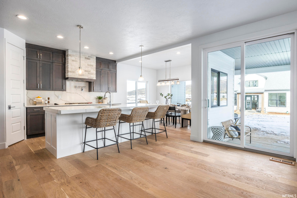Kitchen featuring premium range hood, a breakfast bar area, light hardwood / wood-style flooring, a kitchen island with sink, and pendant lighting