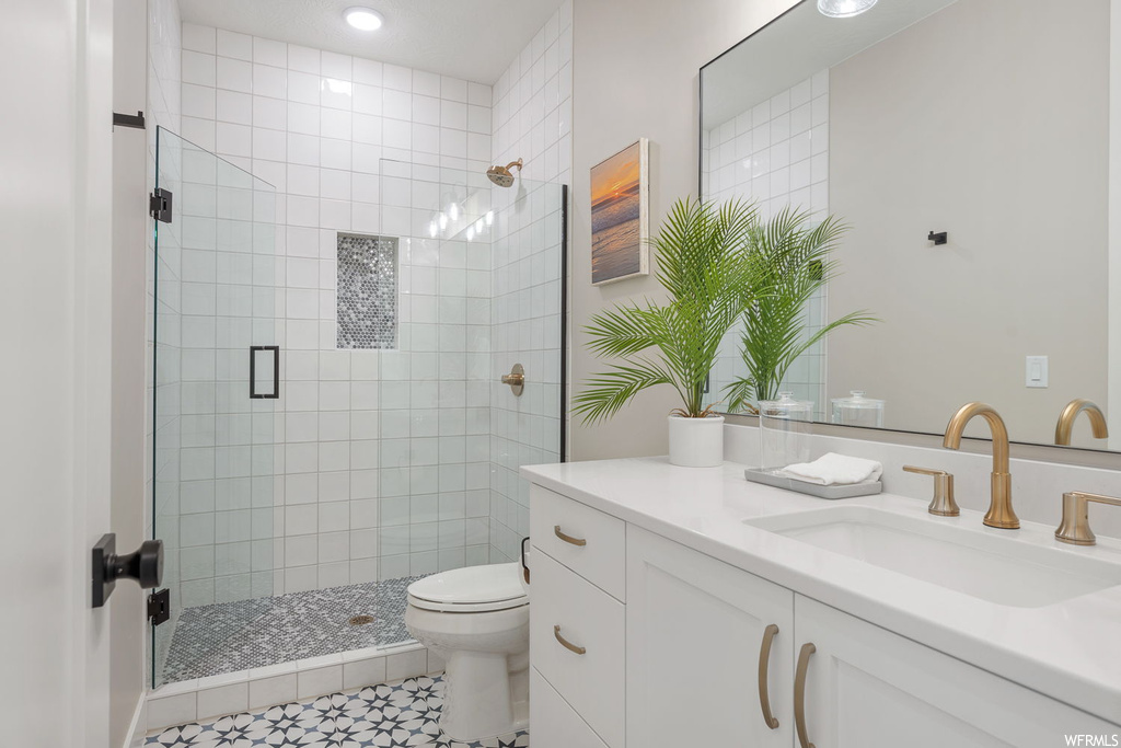 Bathroom featuring toilet, tile floors, a shower with door, and vanity with extensive cabinet space
