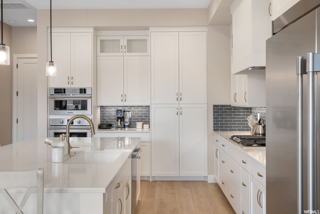 Kitchen with light hardwood / wood-style flooring, hanging light fixtures, stainless steel appliances, white cabinets, and tasteful backsplash