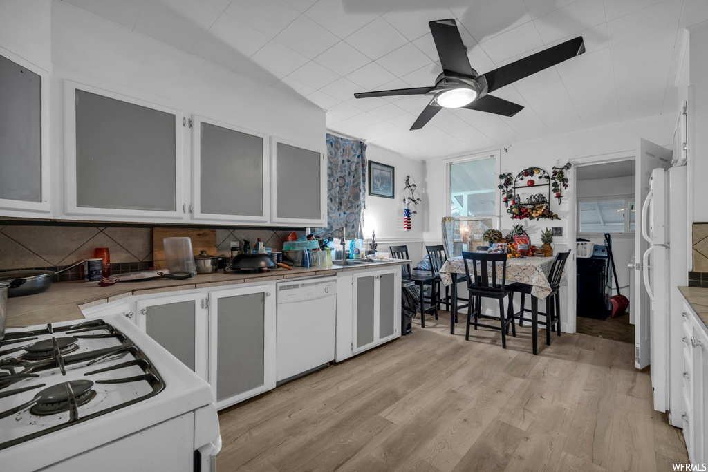 Kitchen with light wood-type flooring, white appliances, ceiling fan, and backsplash