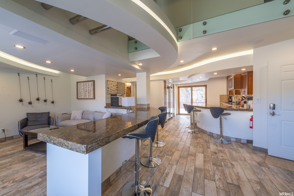 Kitchen featuring a kitchen bar, tasteful backsplash, light hardwood / wood-style floors, and dark stone counters