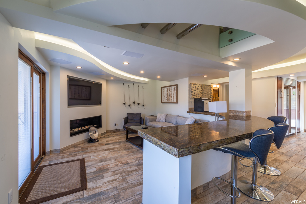 Kitchen with a kitchen breakfast bar, dark stone countertops, and light hardwood / wood-style flooring
