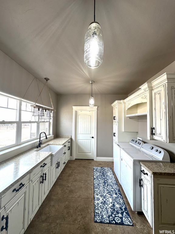 Kitchen with sink, dark tile flooring, washer and clothes dryer, and decorative light fixtures