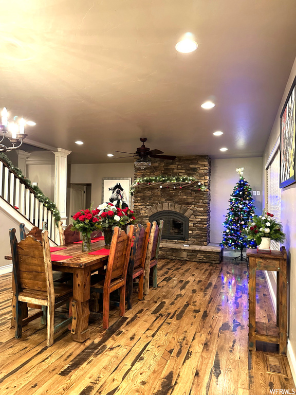 Dining space featuring a stone fireplace, light hardwood / wood-style floors, and ceiling fan with notable chandelier