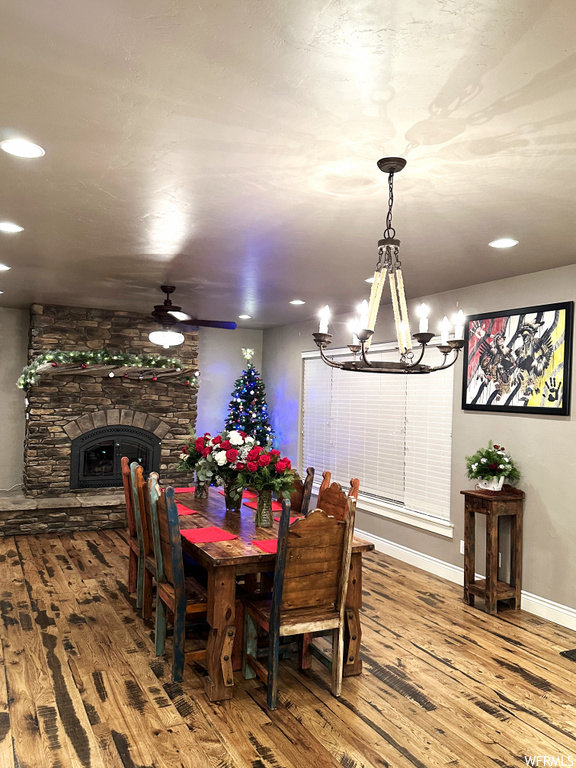 Dining area featuring a fireplace, ceiling fan with notable chandelier, and hardwood / wood-style flooring