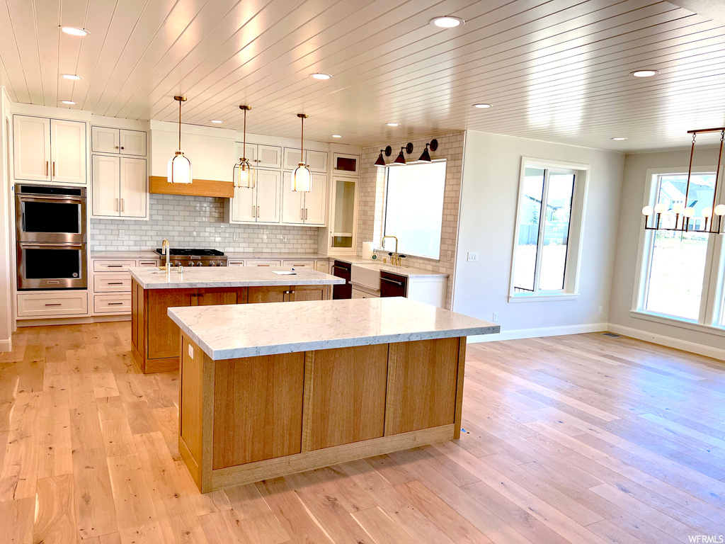 Kitchen featuring backsplash, an island with sink, double oven, and light hardwood / wood-style floors