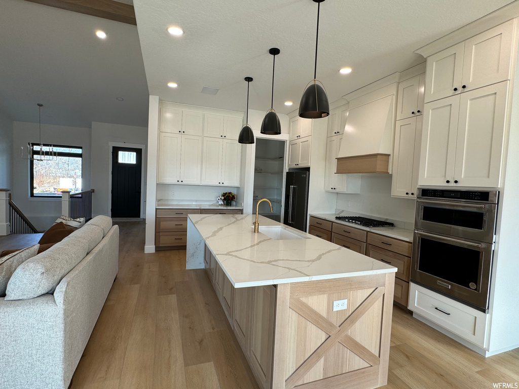 Kitchen featuring sink, light hardwood / wood-style floors, custom exhaust hood, stainless steel appliances, and a spacious island