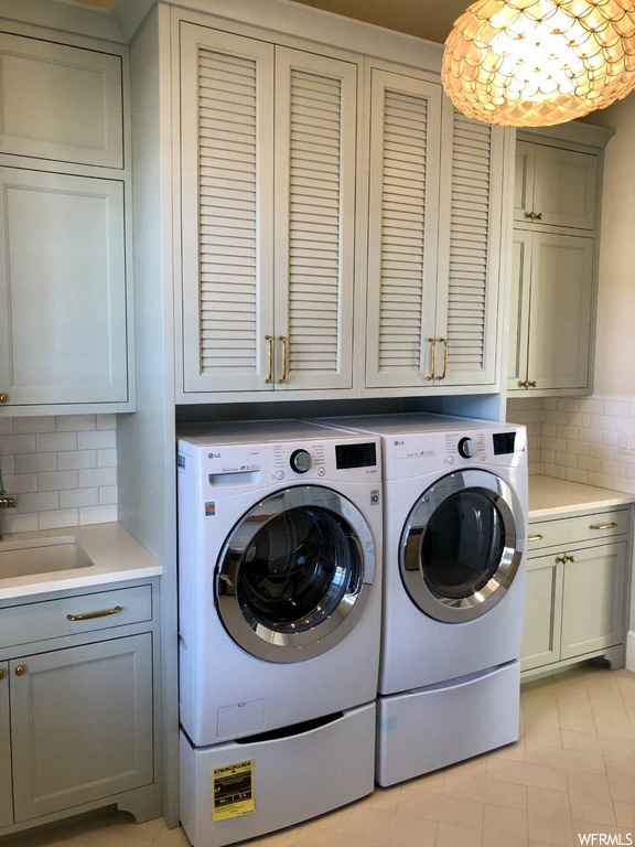 Washroom featuring washer and clothes dryer, cabinets, sink, and light tile floors