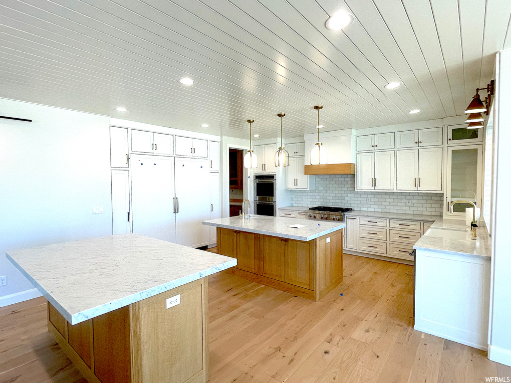 Kitchen with a center island, light wood-type flooring, white cabinetry, and backsplash