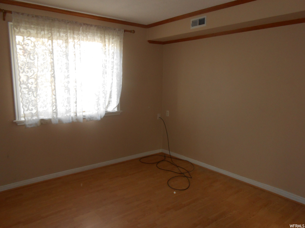 Spare room featuring ornamental molding, a wealth of natural light, and hardwood / wood-style flooring