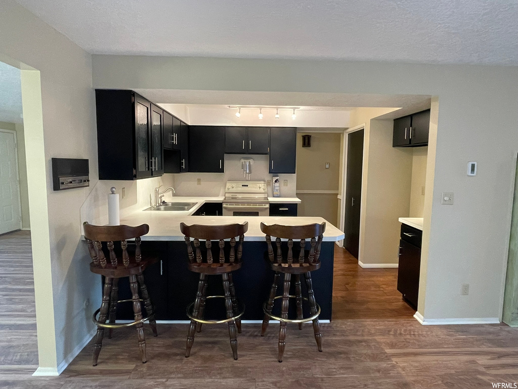Kitchen featuring sink, dark hardwood / wood-style floors, kitchen peninsula, track lighting, and white electric range oven