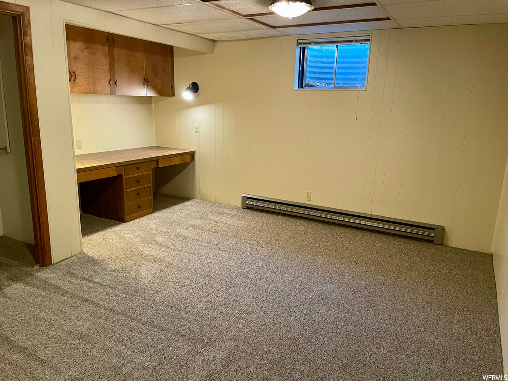 Basement featuring built in desk, baseboard heating, a paneled ceiling, and carpet