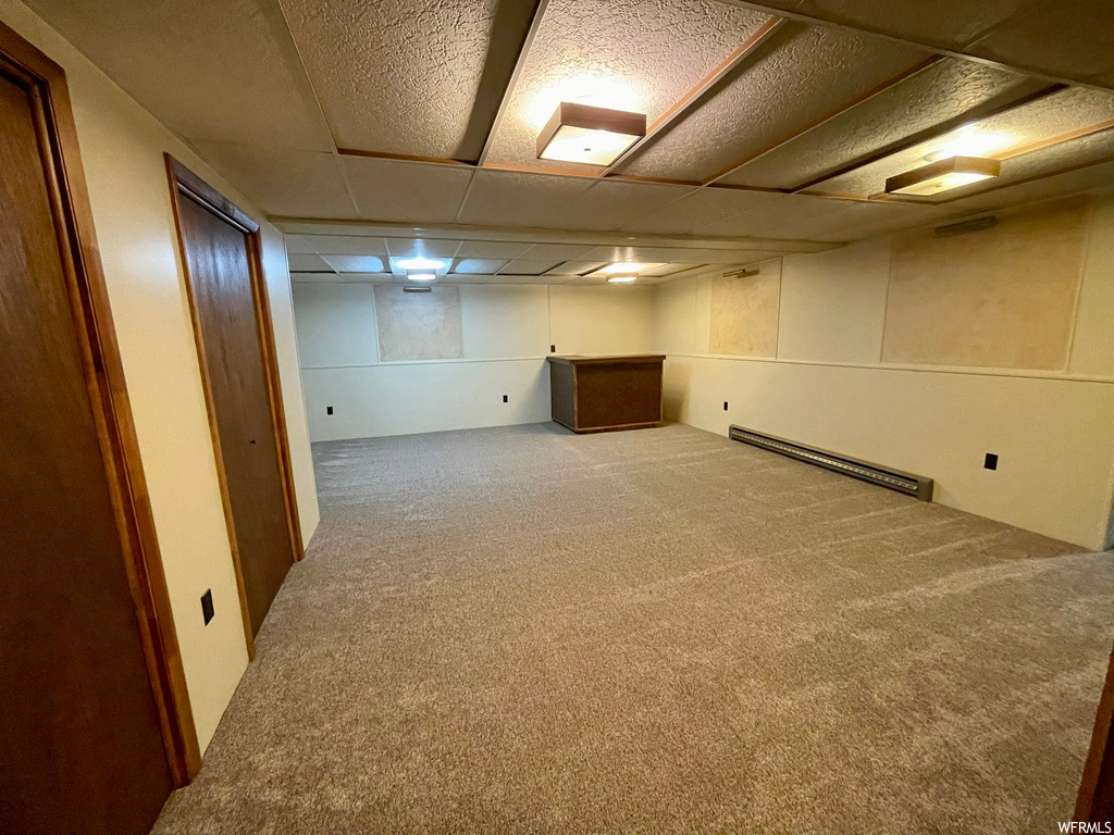 Basement featuring a baseboard radiator, a drop ceiling, and light carpet