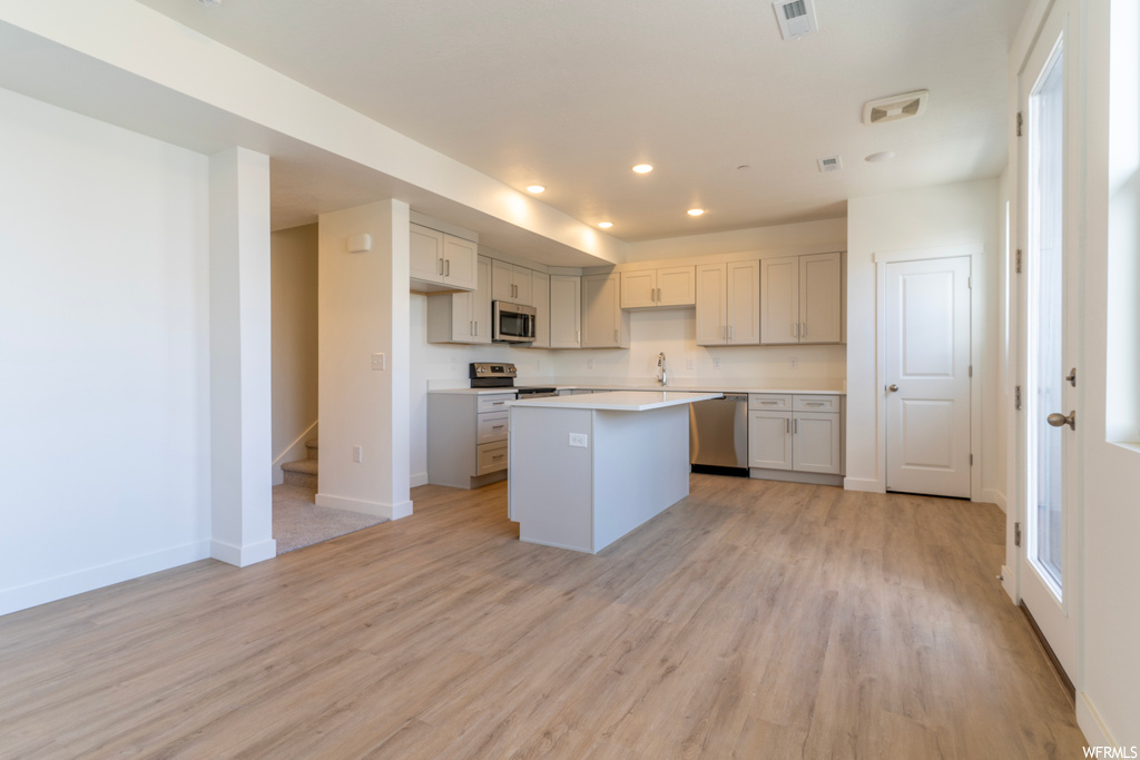 Kitchen featuring sink, light hardwood / wood-style floors, stainless steel appliances, white cabinets, and a kitchen island