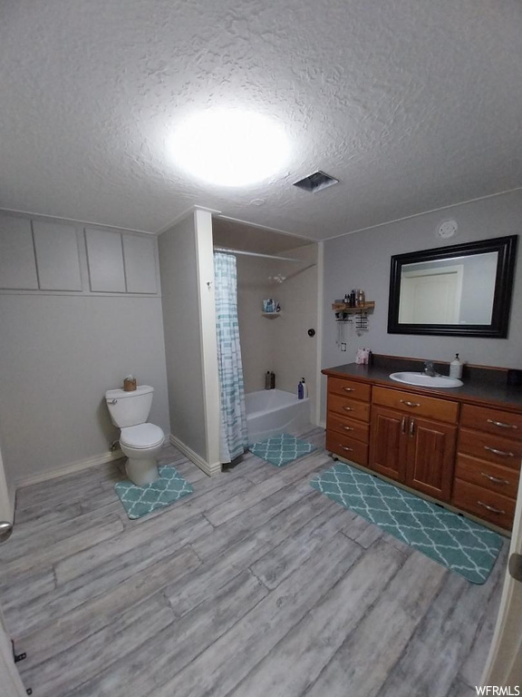 Full bathroom with toilet, a textured ceiling, wood-type flooring, and vanity with extensive cabinet space