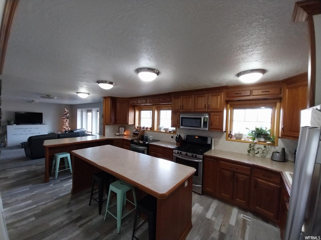 Kitchen with a center island, a textured ceiling, hardwood / wood-style flooring, a kitchen breakfast bar, and appliances with stainless steel finishes