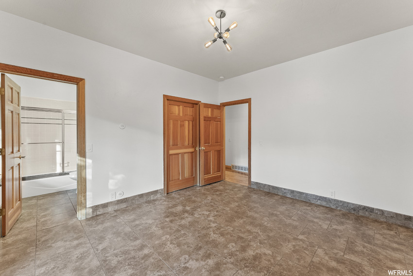 Unfurnished bedroom featuring light tile floors and a notable chandelier