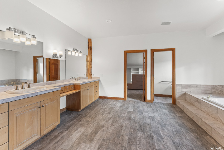 Bathroom with tiled bath, hardwood / wood-style flooring, and dual bowl vanity