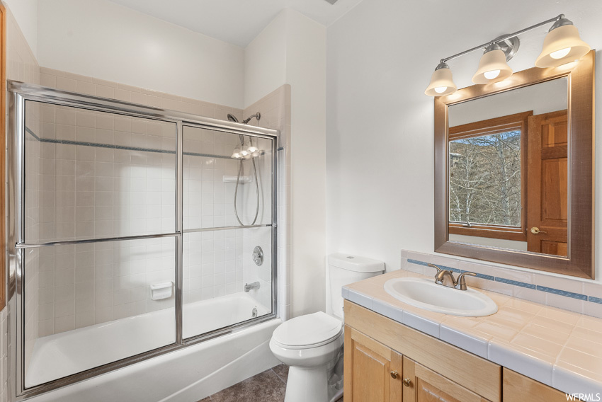 Full bathroom with toilet, enclosed tub / shower combo, and vanity