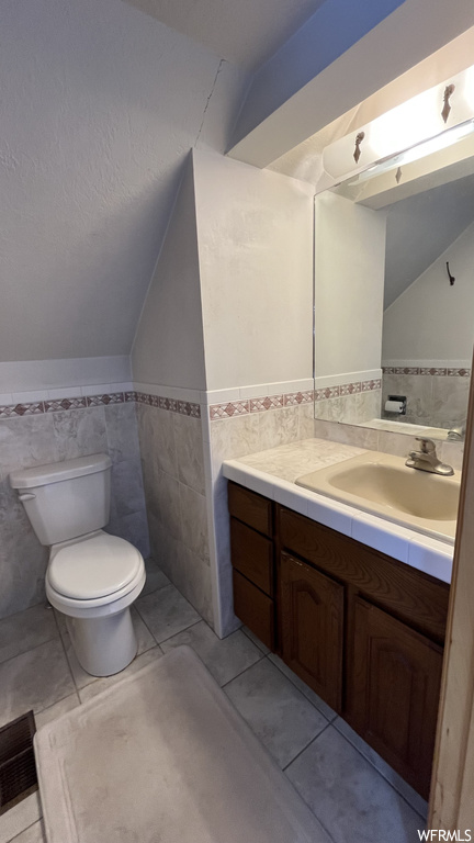 Bathroom featuring toilet, tile walls, tile flooring, lofted ceiling, and vanity