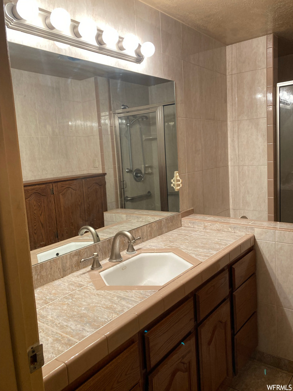 Bathroom with tile walls, a textured ceiling, a shower with door, tile floors, and vanity with extensive cabinet space