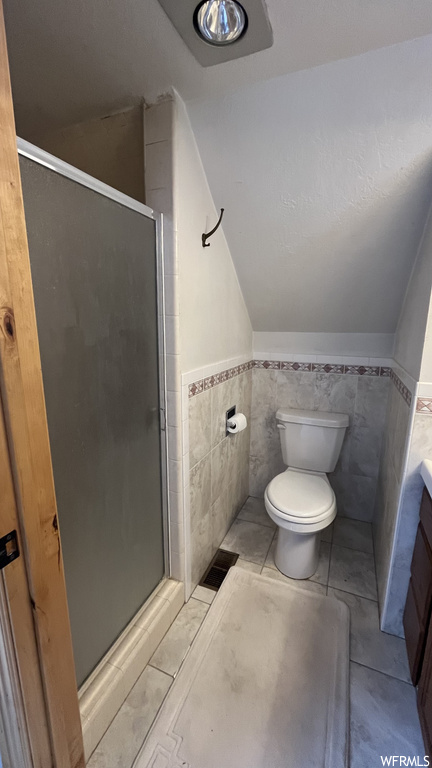 Bathroom featuring toilet, tile walls, tile flooring, a shower with door, and vanity