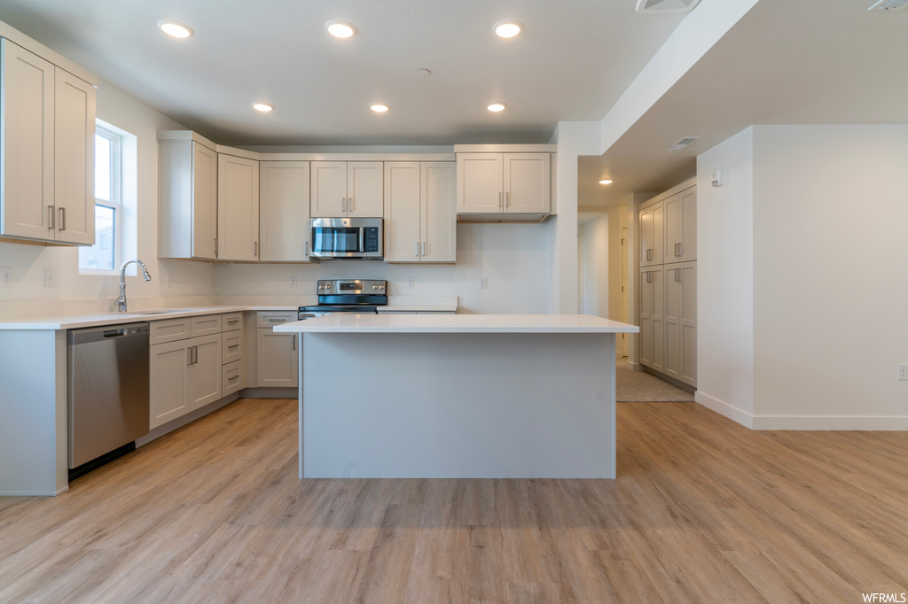 Kitchen with light wood-type flooring, appliances with stainless steel finishes, a kitchen island, and white cabinets