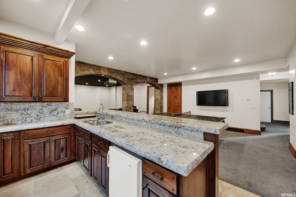 Kitchen featuring sink, light stone counters, kitchen peninsula, light colored carpet, and backsplash