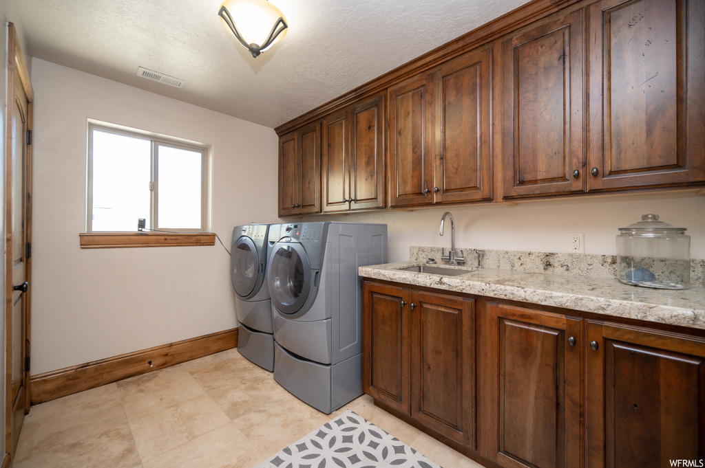 Clothes washing area with independent washer and dryer, sink, a textured ceiling, light tile flooring, and cabinets