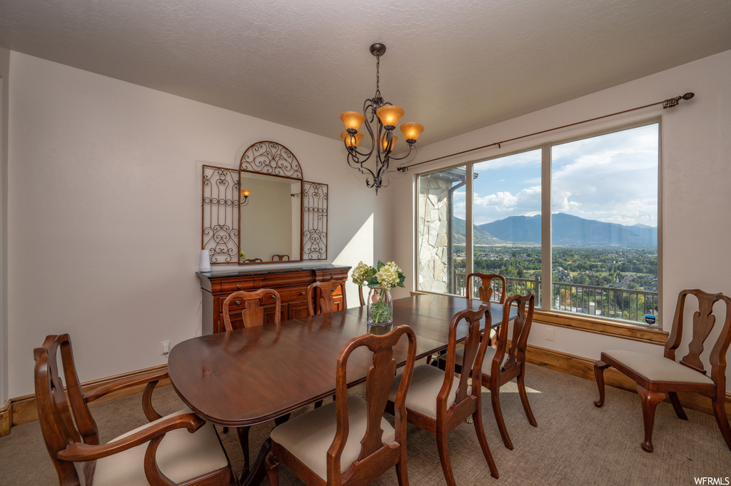 Dining space with a wealth of natural light, light colored carpet, a chandelier, and a mountain view