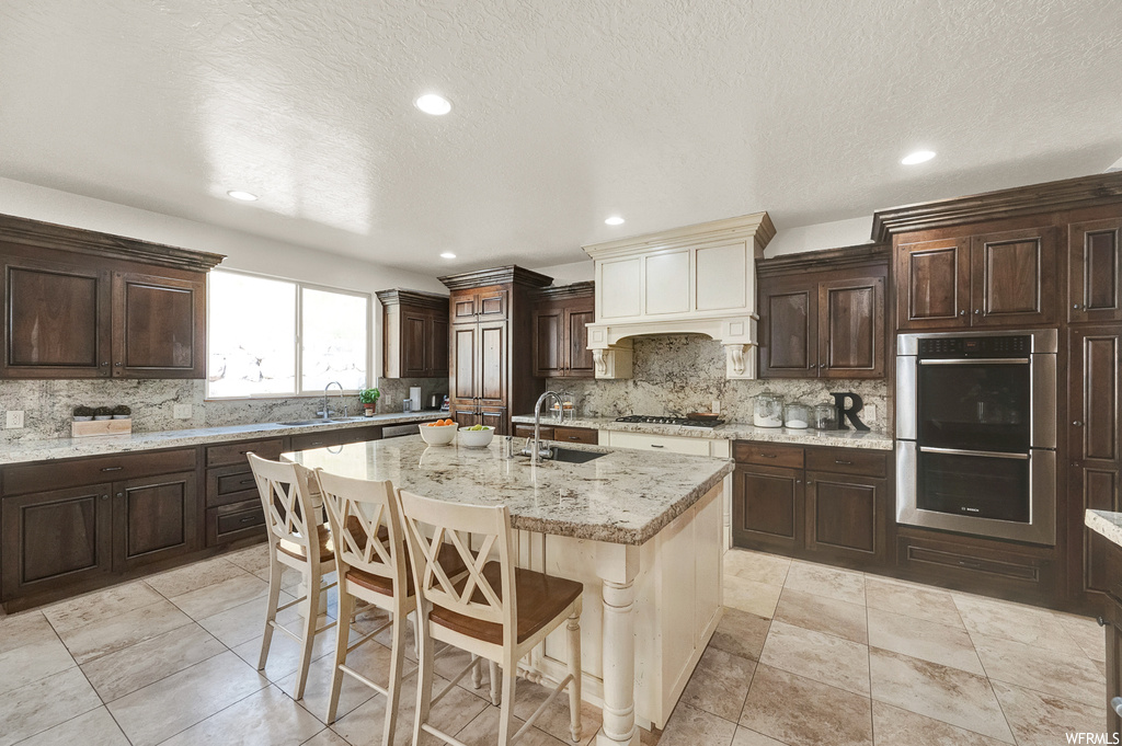Kitchen featuring sink, a kitchen breakfast bar, light stone countertops, stainless steel double oven, and backsplash