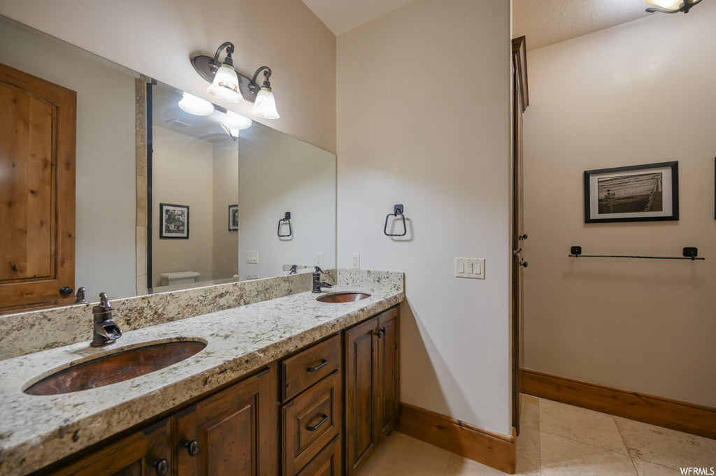 Bathroom with toilet, tile flooring, large vanity, and dual sinks