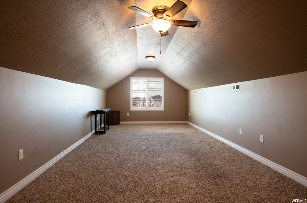 Bonus room with lofted ceiling, ceiling fan, a textured ceiling, and carpet