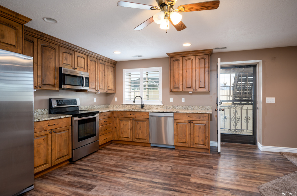 Kitchen featuring dark hardwood / wood-style flooring, appliances with stainless steel finishes, ceiling fan, and light stone countertops