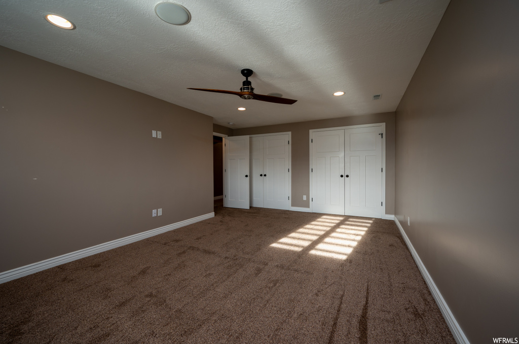 Unfurnished bedroom featuring ceiling fan, a textured ceiling, carpet, and two closets
